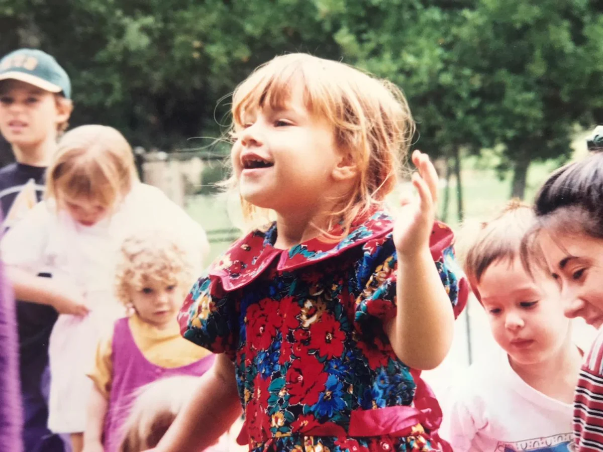 Zoe as a child in São Paulo, laughing, wearing a colourful floral dress